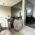 lavabo exento de piedra de río, en un baño con espejo redondo y lámparas colgantes