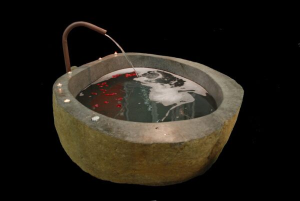 Stone Round Bathtubs Bad van riviersteen, gevuld met water, met rode bloemblaadjes in het water, tegen een zwarte achtergrond